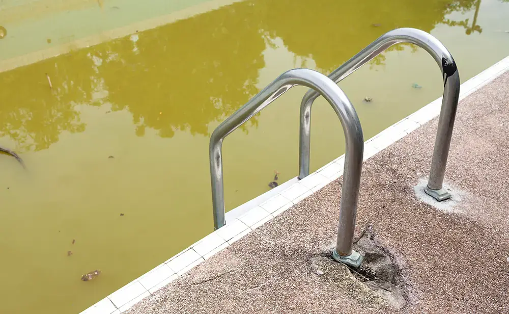 Cracked concrete at the based of a metal rung of a pool ladder