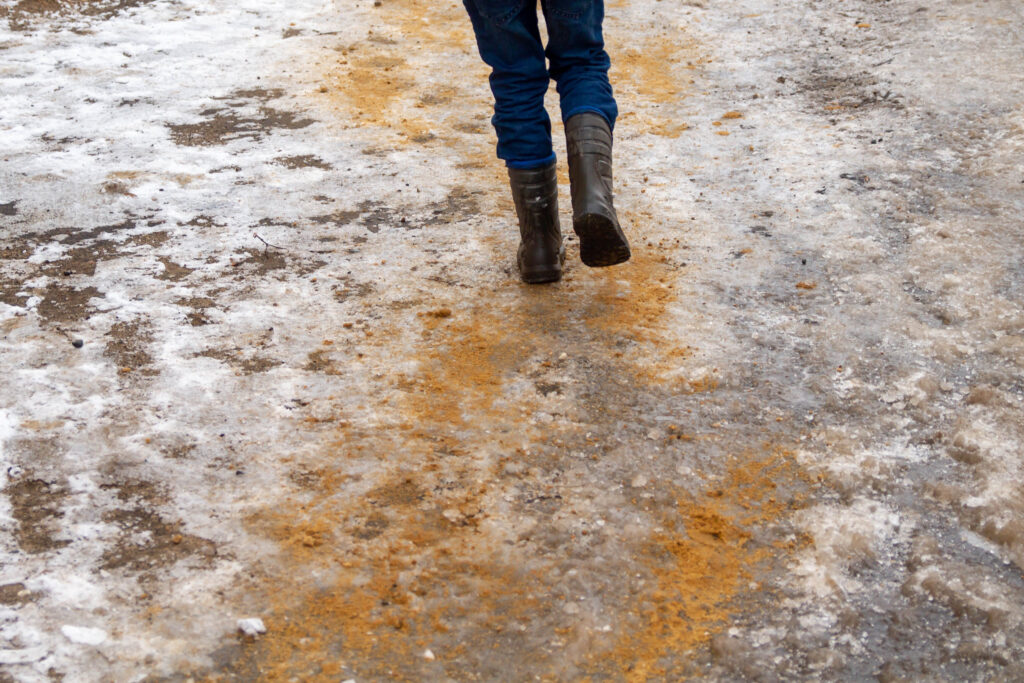 A person stands on icy concrete that has been sprinkled with sand for added traction