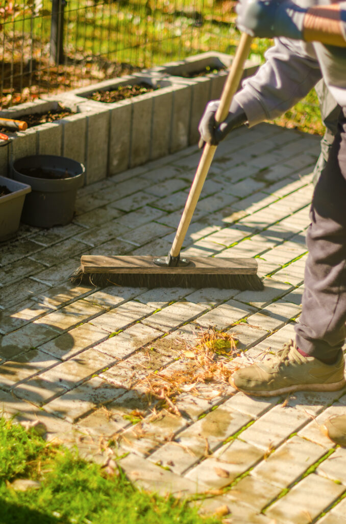 A person is sweeping leaves off of a concrete paver patio