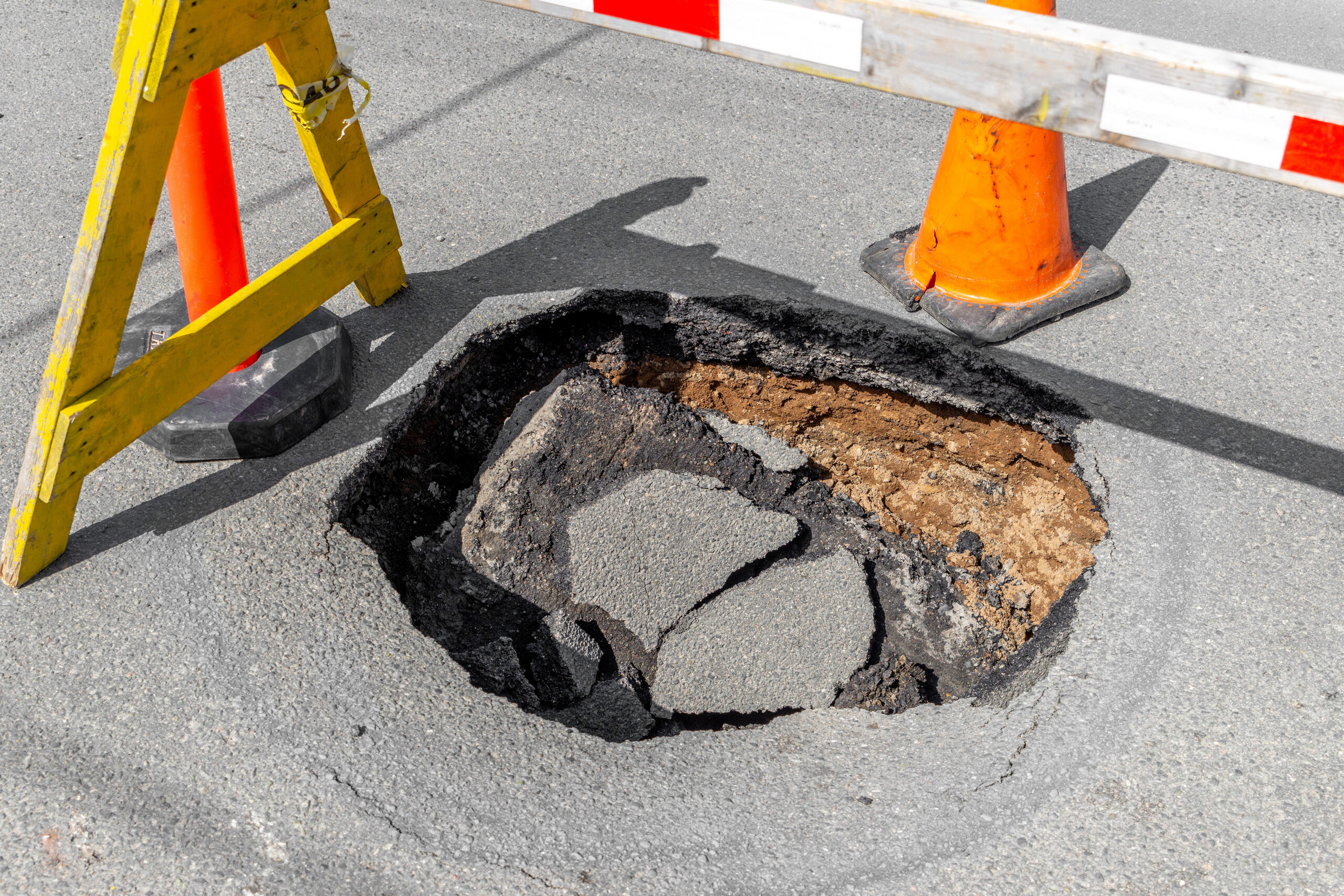 A large pothole blocked off with a traffic cone and sawhorse